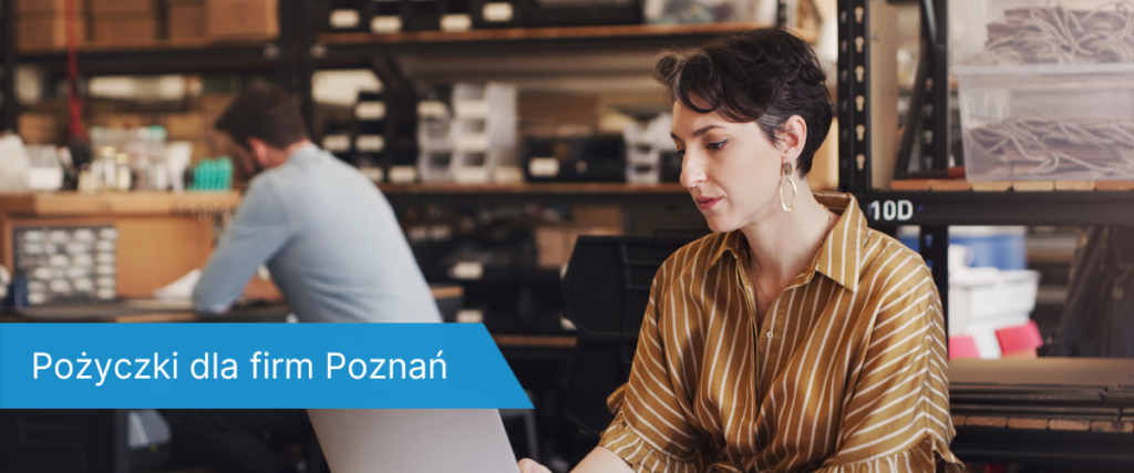 Kobieta w siedzi przy laptopie w przestrzeni magazynowej, w tle mężczyzna pracujący przy stole